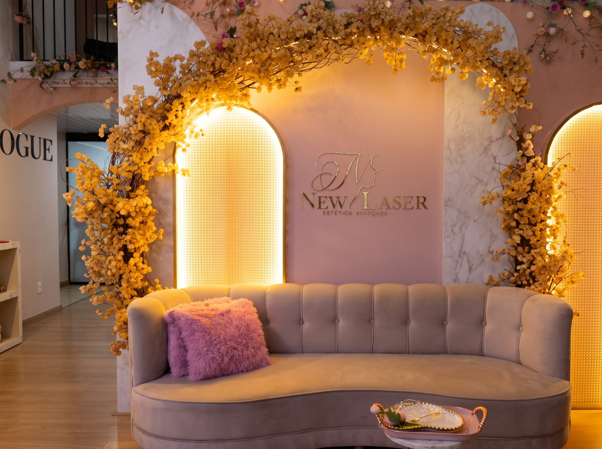 Espaço interno da clínica New Laser Estética Avançada, Toledo/PR — sofá, flores douradas e iluminação acolhedora